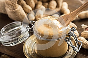 Organic Peanut Butter in Glass Jar with Peanuts in Shell on Wooden Background