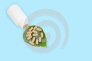 Organic pills on green leaf and jar on blue background