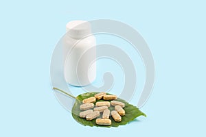 Organic pills on green leaf and jar on blue background