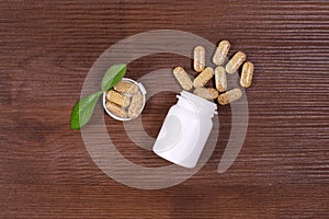 Organic pills on green leaf and jar on wooden background