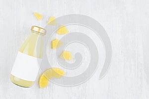Organic pinapple yellow juice in glass bottle with blank label, sliced fruit on white wood background, top view, copy space.