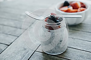 Organic Pudding with chia seeds and spoon, yogurt and fresh fruits: Strawberries, blueberries and blackberries in glass jars on w