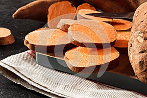 Organic raw sweet potato whole and sliced on wooden kitchen board. Rustic style