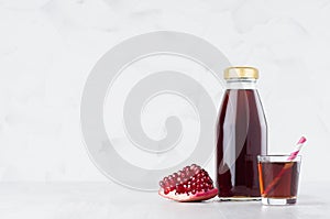 Organic red garnet juice juice in glass bottle mock up with straw, wine glass, fruit slice on white wood table in light interior.