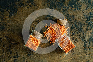 Organic red lentil in little glass bottles on abstract wooden background. Top view