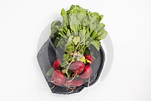 Organic red radish in eco friendly reusable produce bag, white background