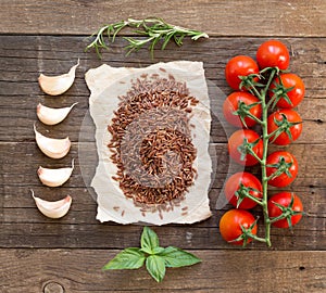 Organic red rice, tomatoes, garlic and herbs on wooden background