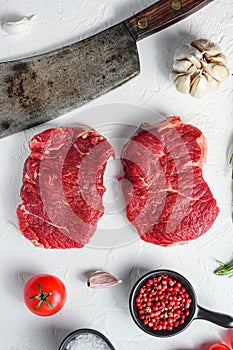 Organic rump steak, raw beef meat with seasonings, rosemary, garlic and butcher cleaver. White textured background. Top view