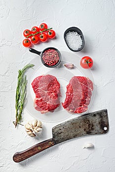 Organic rump steak, raw beef meat with seasonings, rosemary, garlic and butcher cleaver. White textured background. Top view