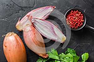 Organic shallot, bio eschalot or farm scallion raw ripe onions with greens and rose peppercorns sliced and halved black concrete