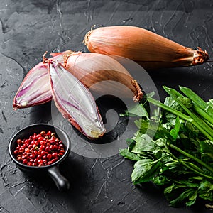 Organic shallot, bio eschalot or farm scallion raw ripe onions with greens and rose peppercorns sliced and halved black concrete