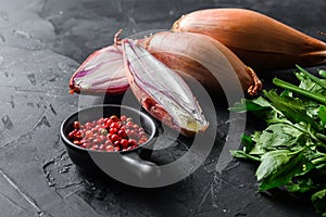 Organic shallot, eschalot or scallion raw ripe onions with greens and rose peppercorns sliced and halved black concrete textured