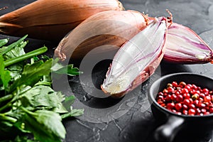 Organic shallot, eschalot or scallion raw ripe onions with greens and rose peppercorns sliced and halved black concrete textured