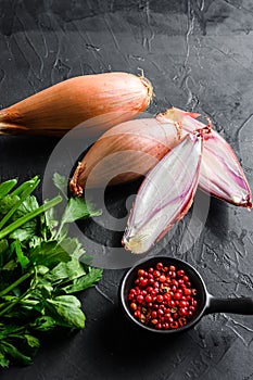 Organic shallot, eschalot or scallion raw ripe onions with greens and rose peppercorns sliced and halved black concrete textured