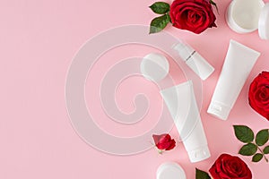 Organic skincare concept. Flat lay composition made of cosmetic tubes with cream without label, red roses on pastel pink backgroun