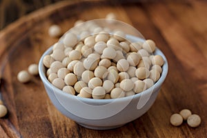 Organic soybeans at white ceramic bowl over wooden table.