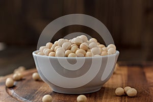 Organic soybeans at white ceramic bowl over wooden table.