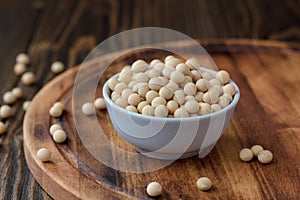 Organic soybeans at white ceramic bowl over wooden table.