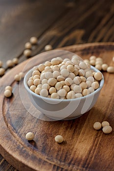Organic soybeans at white ceramic bowl over wooden table.