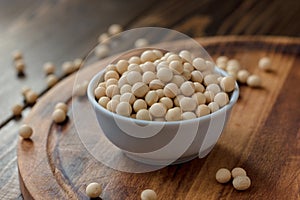 Organic soybeans at white ceramic bowl over wooden table.