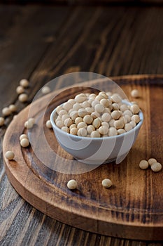 Organic soybeans at white ceramic bowl over wooden table.