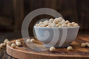 Organic soybeans at white ceramic bowl over wooden table.