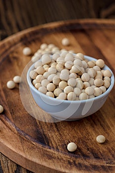 Organic soybeans at white ceramic bowl over wooden table.