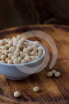 Organic soybeans at white ceramic bowl over wooden table.