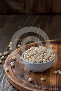 Organic soybeans at white ceramic bowl over wooden table.