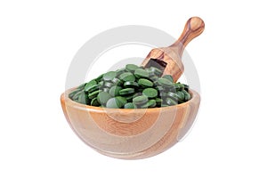 Organic spirulina and chlorella pills in a wooden bowl with a scoop isolated on white