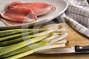 Organic spring onion and raw bacon on a wooden board