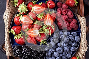 Organic strawberries, raspberries, blueberries, blackberries on a separate dish close-up on a solid concrete background.