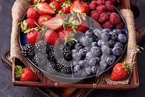 Organic strawberries, raspberries, blueberries, blackberries on a separate dish close-up on a solid concrete background.