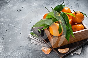 Organic Tangerines, mandarins with green leaves in wooden box. Gray background. Top view. Copy space