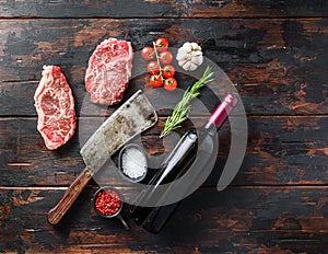 Organic top blade steak, raw beef meat with seasonings, rosemary and butcher cleaver and red wine bottle. Wood textured background