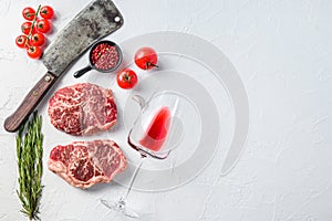 Organic top blade steak, raw beef meat with seasonings, rosemary, garnet, rose wine glass and butcher cleaver. White textured