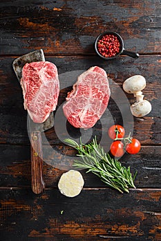 Organic Top blade steak, raw meat, marbled beef butler cut on metal butcher cleaver knife with rosemary and farm herbs over old