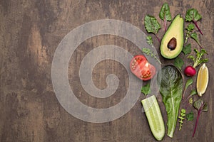 Organic vegetables and herbs on brown abstract background. Copy space, flat lay, top view. Avocado, tomato, green lettuce leaves