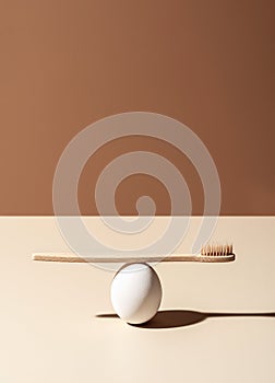 Organic wooden bamboo toothbrush and white egg composition on terracotta and beige background.