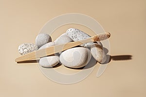 Organic wooden bamboo toothbrush and white sea pebbles on natural beige background.