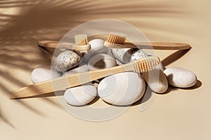 Organic wooden bamboo toothbrush and white sea pebbles on natural beige background with palm leaf shadow.