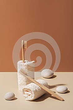 Organic wooden bamboo toothbrushes, towels and white sea pebbles on terracotta and beige background.