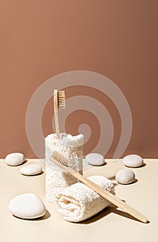 Organic wooden bamboo toothbrushes, towels and white sea pebbles on terracotta and beige background.