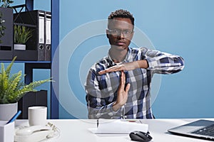 Organization leader gesturing timeout symbol with hands while in office workspace.