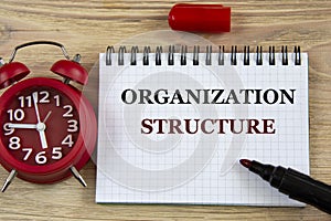 ORGANIZATION STRUCTURE - words in a notebook on a wooden background with an alarm clock and a marker