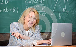 Organize class and make learning easy process. Teacher woman sit table work laptop surfing internet chalkboard