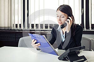 Organized responsible office worker business woman giving instructions via phone call. Looking confused checking notes and paperwo