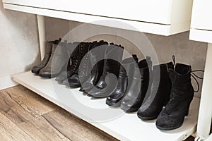 Organized shoe rack, shoe rack with black stylisch shoes and boots, on a wooden floor, besides a white wall. modern room