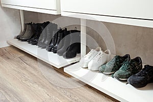 Organized shoe rack, shoe rack with black stylisch shoes and boots, on a wooden floor, besides a white wall. modern room