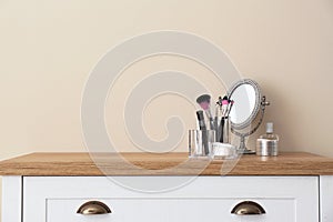 Organizer with makeup cosmetic products and mirror on table against light wall